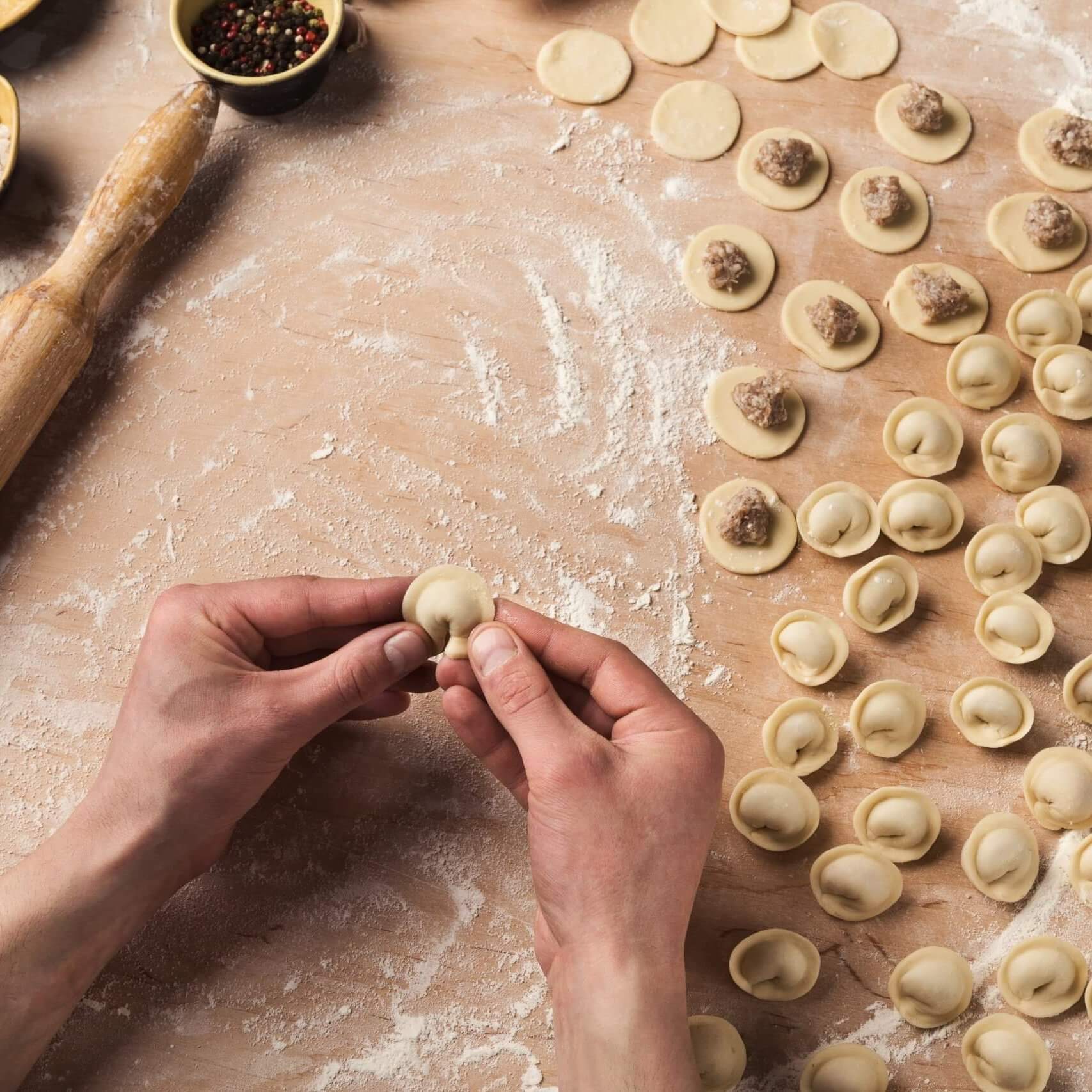 Chef hands forming small handmade dumplings on kitchen table, cooking ingredients, top view